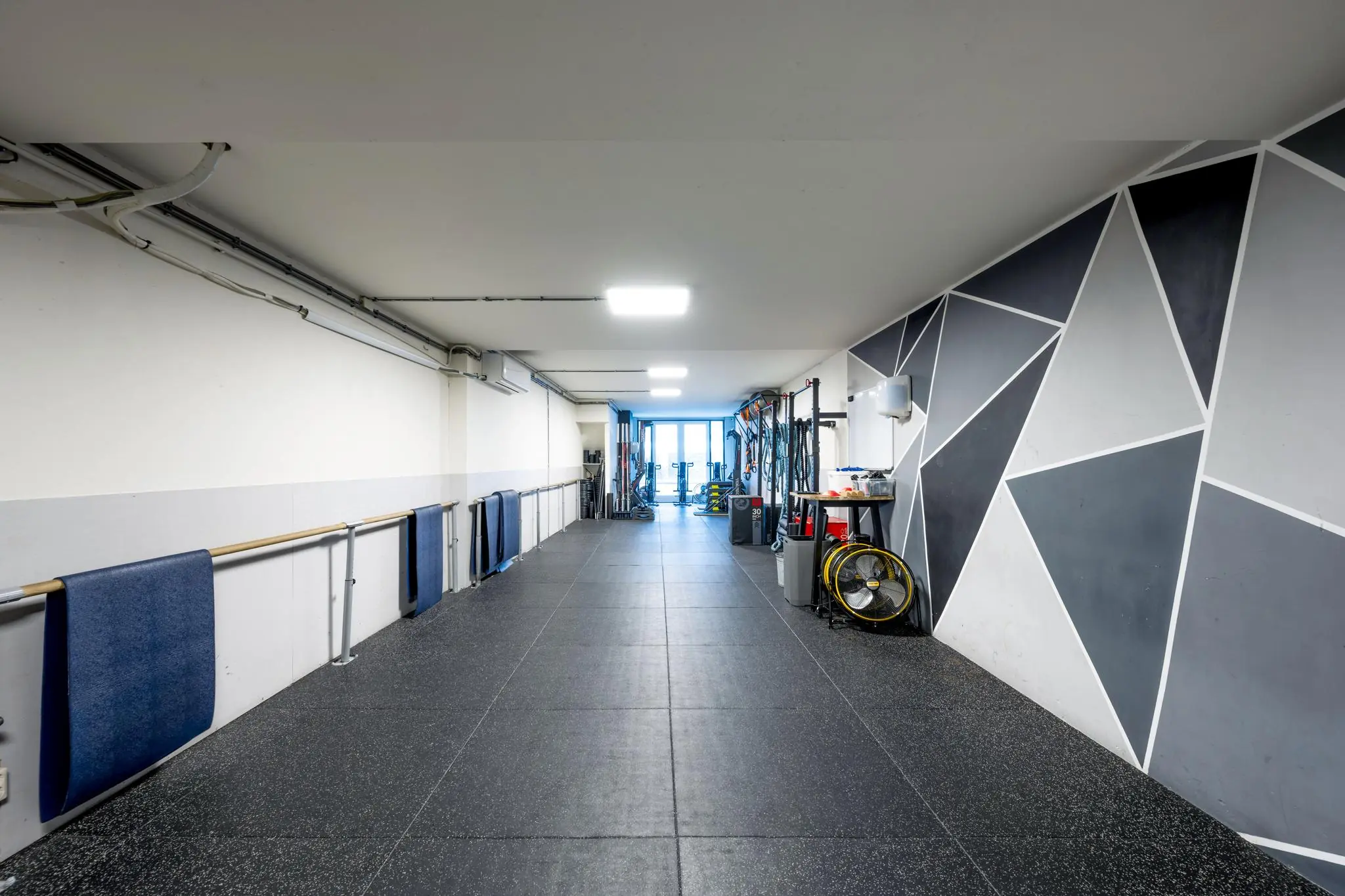 Moderne fitnessruimte aan de Albert Cuypstraat met sportmateriaal en geometrisch gedecoreerde muur.